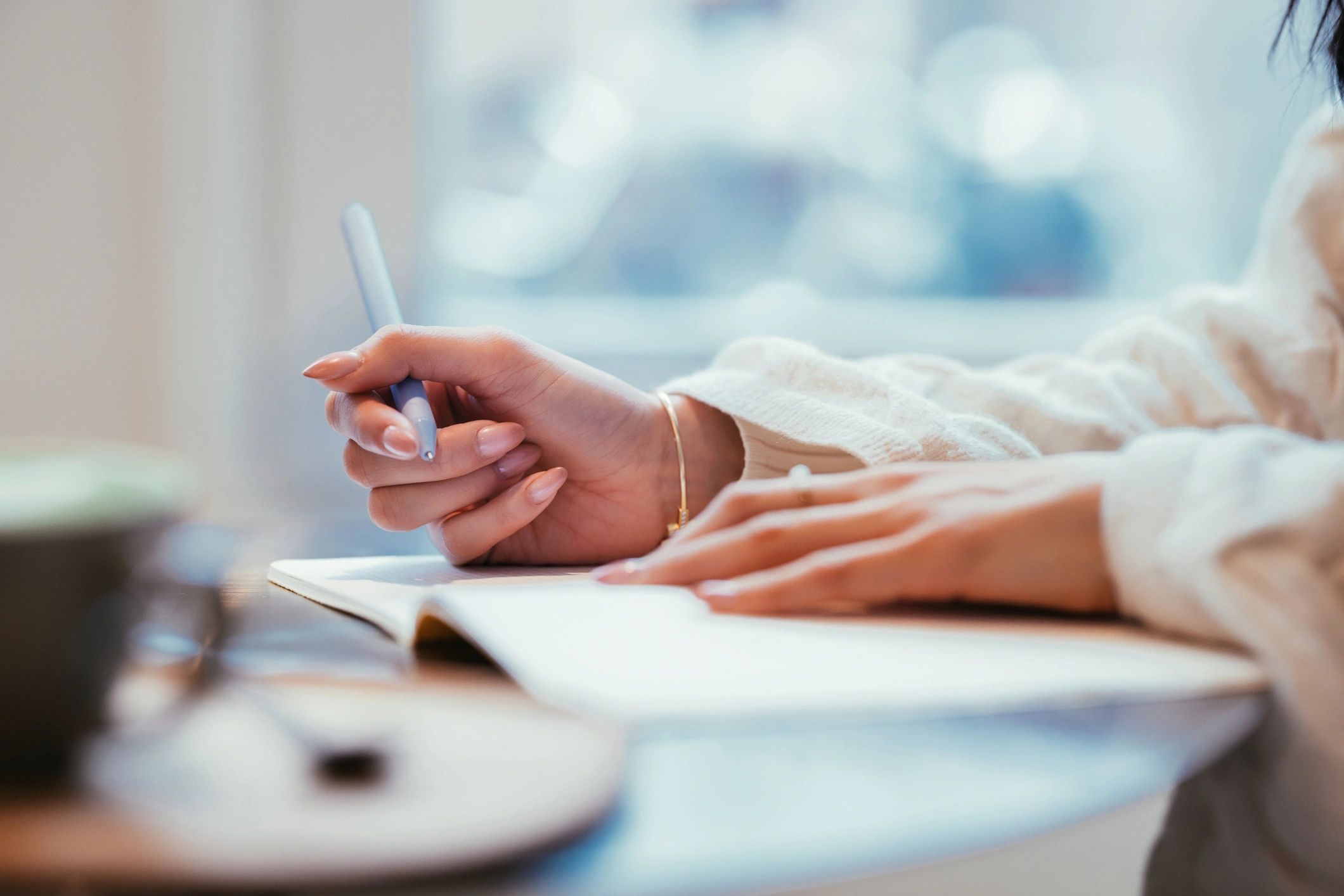 Close-up of a woman writing in a journal beside coffee