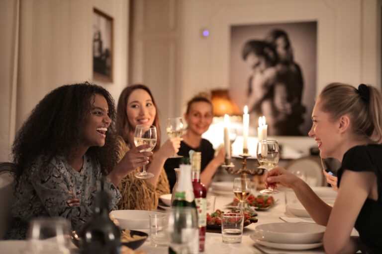 Diverse group of women friends laughing and toasting wine at a candlelit dinner