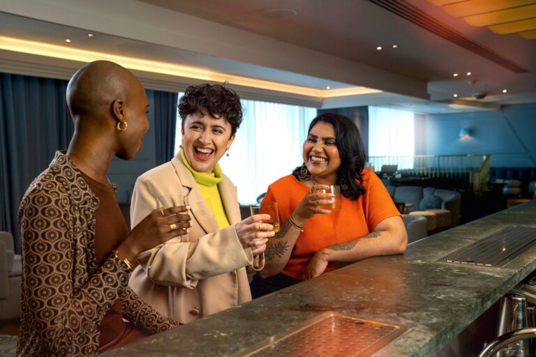 Three diverse women friends laughing and toasting drinks at a bar